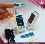 صورة حقيقة بزاوية أمامية لجاهزين بلص اوكسميتر هاند هيلد Yonker Handheld Oximeter على طاولة مع المشتملات، تصميم أبيض صغير بشاشة 2.4 بوصة TFT.