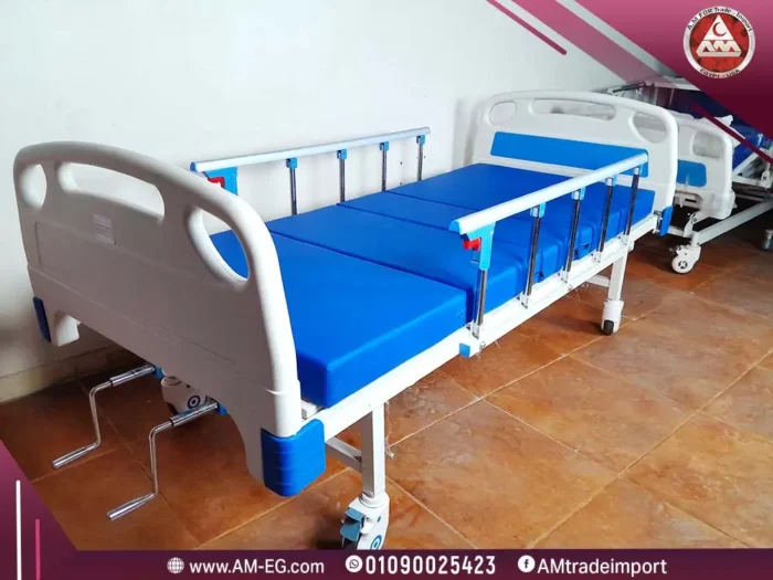صورة طبيعية لسرير طبي 2 حركة يدوي في وضع مسطح، بتصميم معدني أبيض، ومرتبة طبية زرقاء اللون، مع جوانب أمان، وبأربع عجلات.