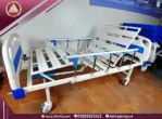 Real image of Manual 2-crank hospital bed fully raised, white metal design, without a mattress, with four wheels and safety side rails
