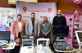 طاقم شركة الأمين ميديكال في قاعة عرض للأجهزة الطبية يٌف خلف مجموعة أجهزة طبية مثل شاشات مراقبة المريض وأجهزة سونار ورسم قلب
